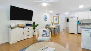 A modern living room with a flat-screen TV, a dining area with a table and chairs, a kitchen with white cabinets and appliances, and a ceiling fan. - Sailfish Suites 8 - Waterfront Lodging (Stuart)