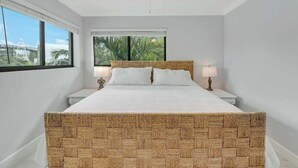 Une chambre avec un grand lit, deux tables de chevet, un ventilateur de plafond et une vue sur les palmiers par la fenêtre.