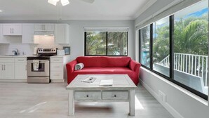 Une cuisine moderne avec des meubles blancs, un canapé rouge, une table basse blanche et une grande fenêtre donnant sur des palmiers.