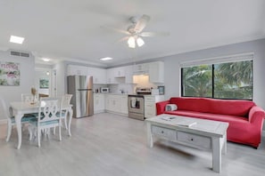 A modern kitchen with white cabinets, a red sofa, and a dining area with white chairs. - Sailfish Suites - 12 - waterfront lodging (Stuart)