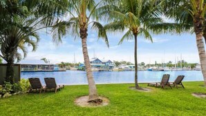 A poolside area with two lounge chairs and a palm tree, overlooking a marina with boats. - Sailfish Suites - 11 - Waterfront (Stuart)