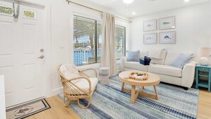 A modern living room with a white sofa, a round wooden coffee table, a wicker chair, and a ceiling fan. - Sailfish Suites - 11 - Waterfront (Stuart)