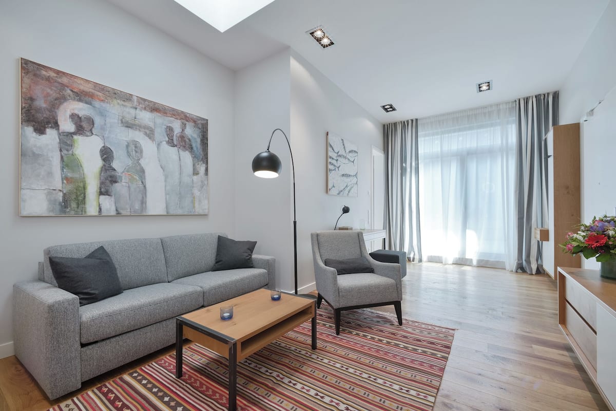 Ein modernes Wohnzimmer mit einem grauen Sofa, einem Holztisch, einem gemusterten Teppich und einem großen abstrakten Gemälde an der Wand.