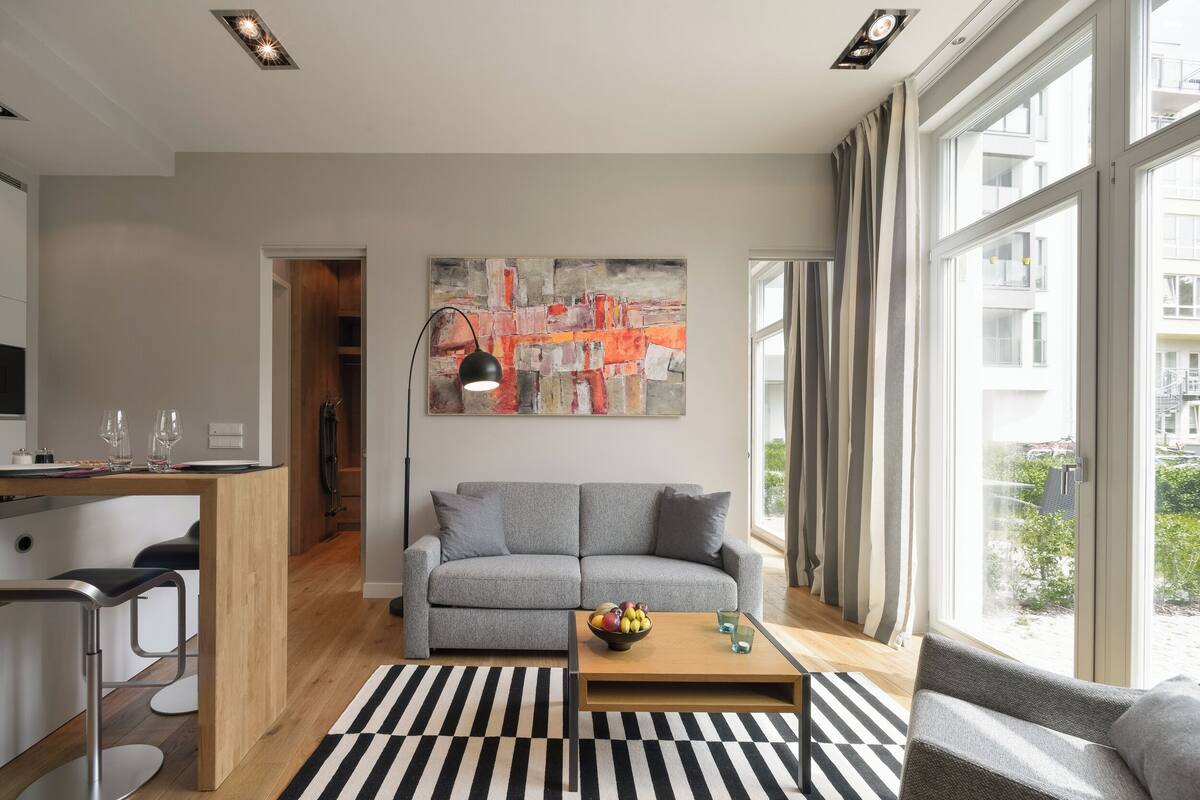 Ein modernes Wohnzimmer mit einem grauen Sofa, einem Holztisch und einem schwarz-weißen Teppich.
