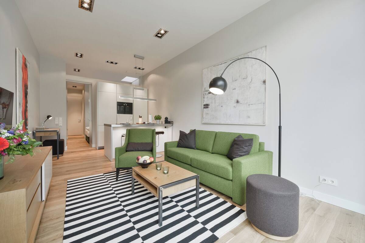 Ein modernes Wohnzimmer mit einem grünen Sofa, einem Couchtisch und einem schwarz-weiß gestreiften Teppich.