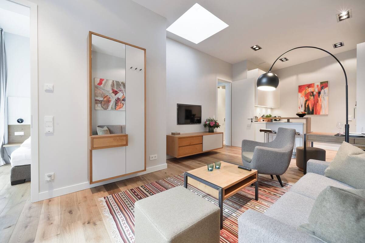 Ein modernes Wohnzimmer mit Sofa, Sessel, Couchtisch und Fernseher auf einer Holzkommode.