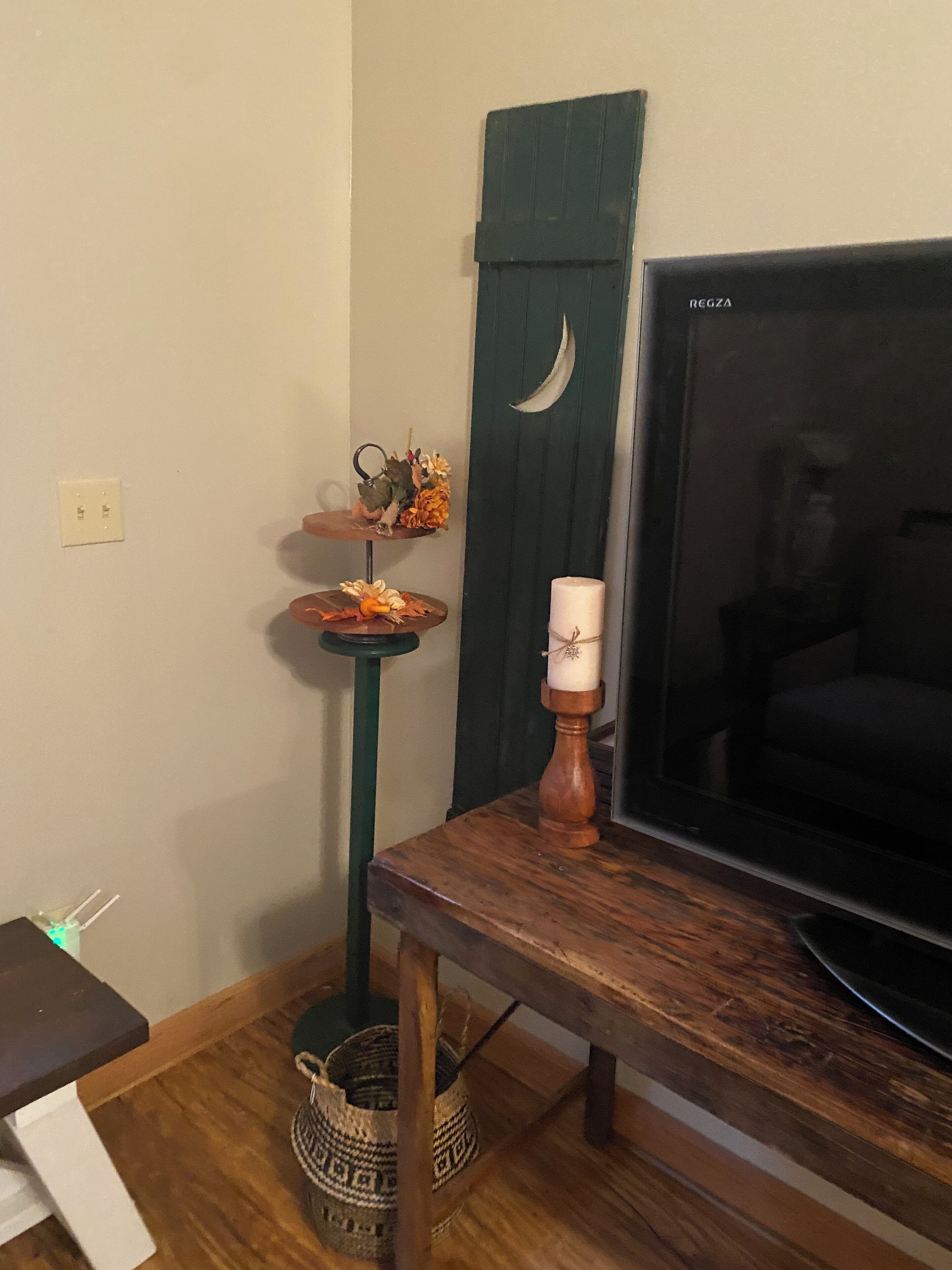 Een kamer met een houten tafel, een televisie, een decoratieve plank met bloemen, een kaars en een mand.