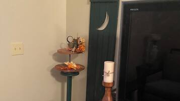 Een kamer met een houten tafel, een televisie, een decoratieve plank met bloemen, een kaars en een mand.