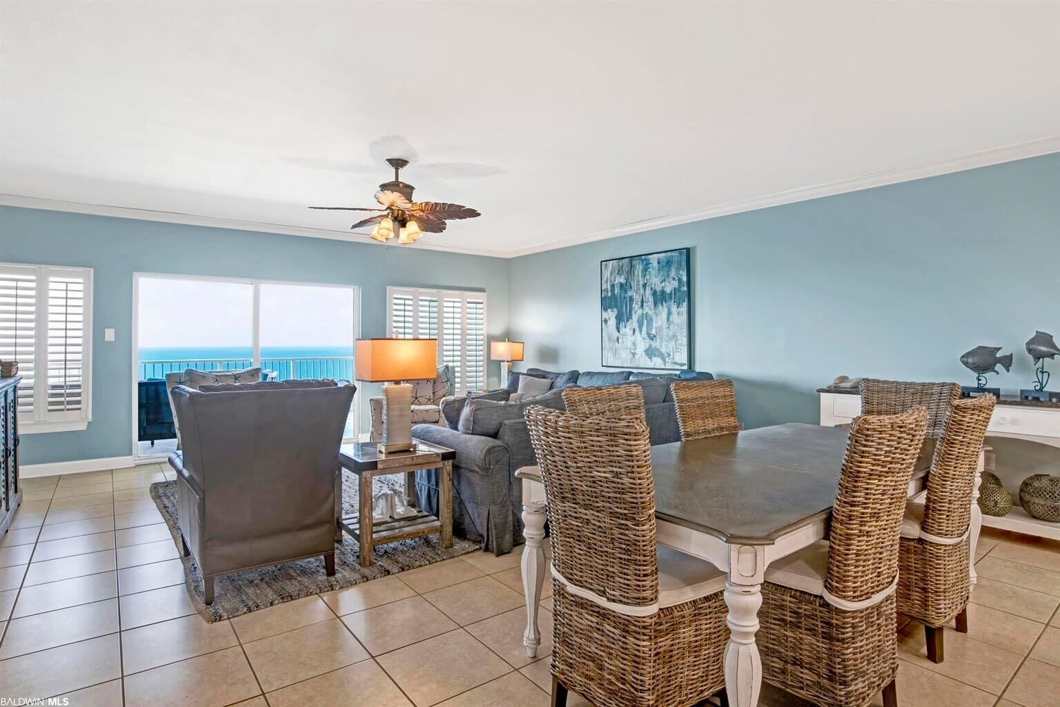 A spacious living room with a dining area, large windows, and a ceiling fan.