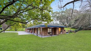 A single-story house with a brick exterior and a blue roof, surrounded by a well-maintained lawn and trees. - Tree-Lined Donvale Nature Family Getaway (Donvale)