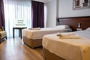 Ett hotellrum med tvÄ sÀngar, ett nattduksbord, en stol och en skylt som visar hotellets namn.
