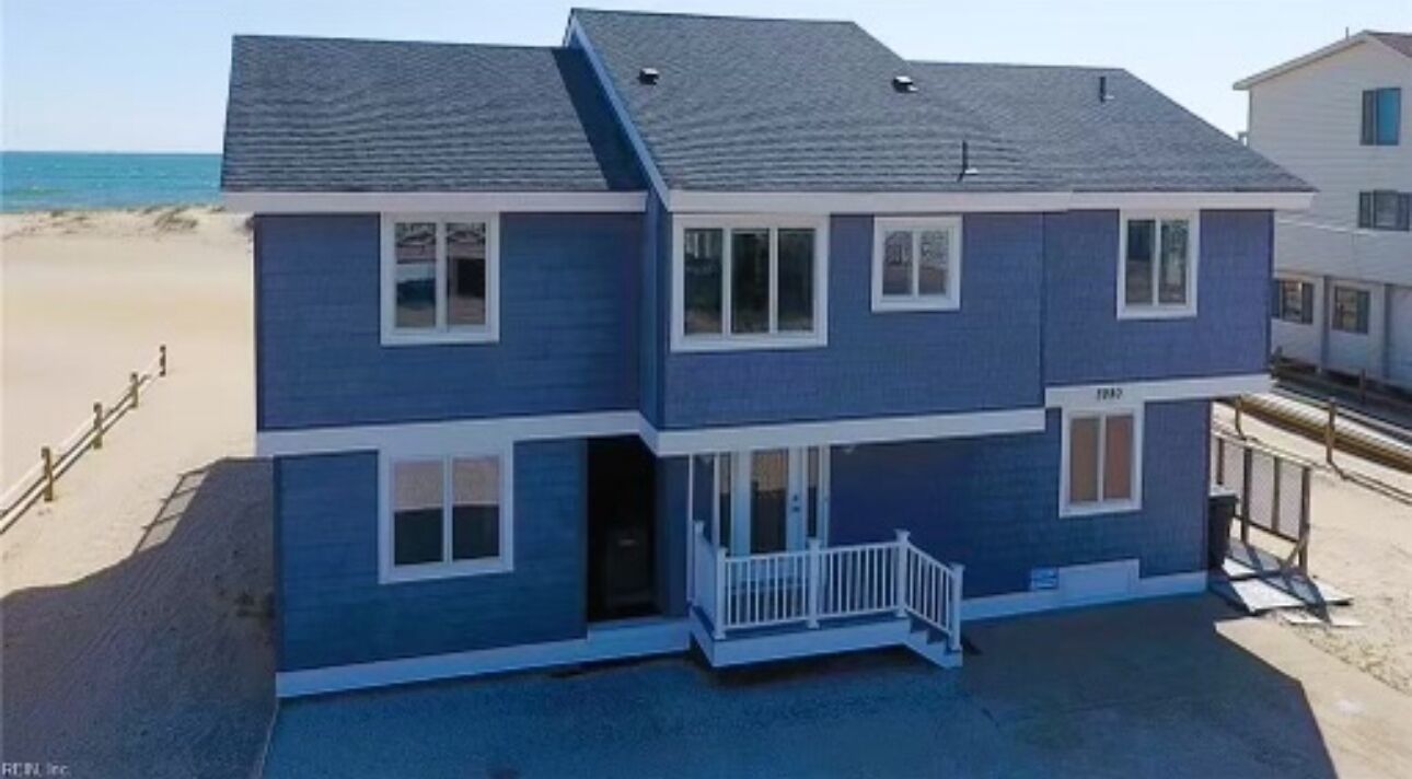 A two-story house with a balcony, located near a beach.
