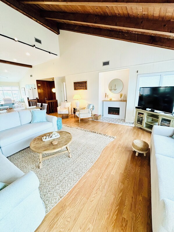 A spacious living room with a high ceiling, a fireplace, a television, and a dining area. - Oceanfront home “Sea Watch” with beautiful new pool (Virginia Beach)