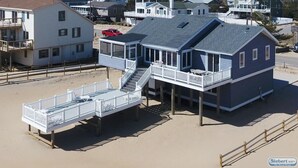 Una casa frente a la playa con un balcón y una pequeña terraza, conectadas por una escalera.