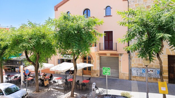 Un edificio de fachada rosa, una puerta con persiana cerrada y un cartel de estacionamiento verde.