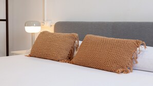 Una cama con dos almohadones marrones de punto y una mesita de noche blanca con una lámpara.