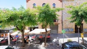Un café al aire libre con mesas y sillas, un edificio de fachada de piedra y un árbol en primer plano.