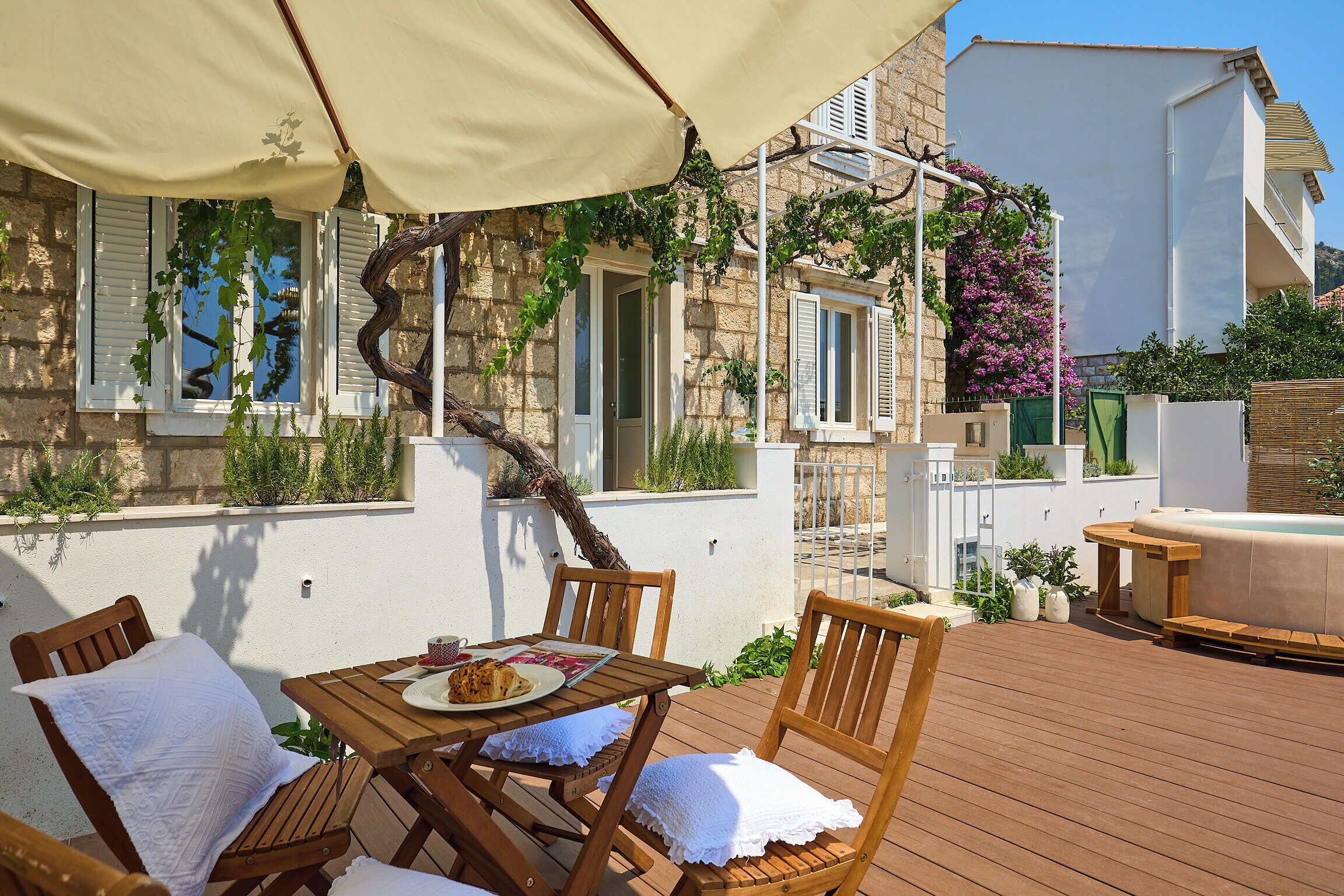 Eine Holzterrasse im Freien mit Tisch und Stühlen, ein überdachter Bereich mit Tisch sowie ein Whirlpool.