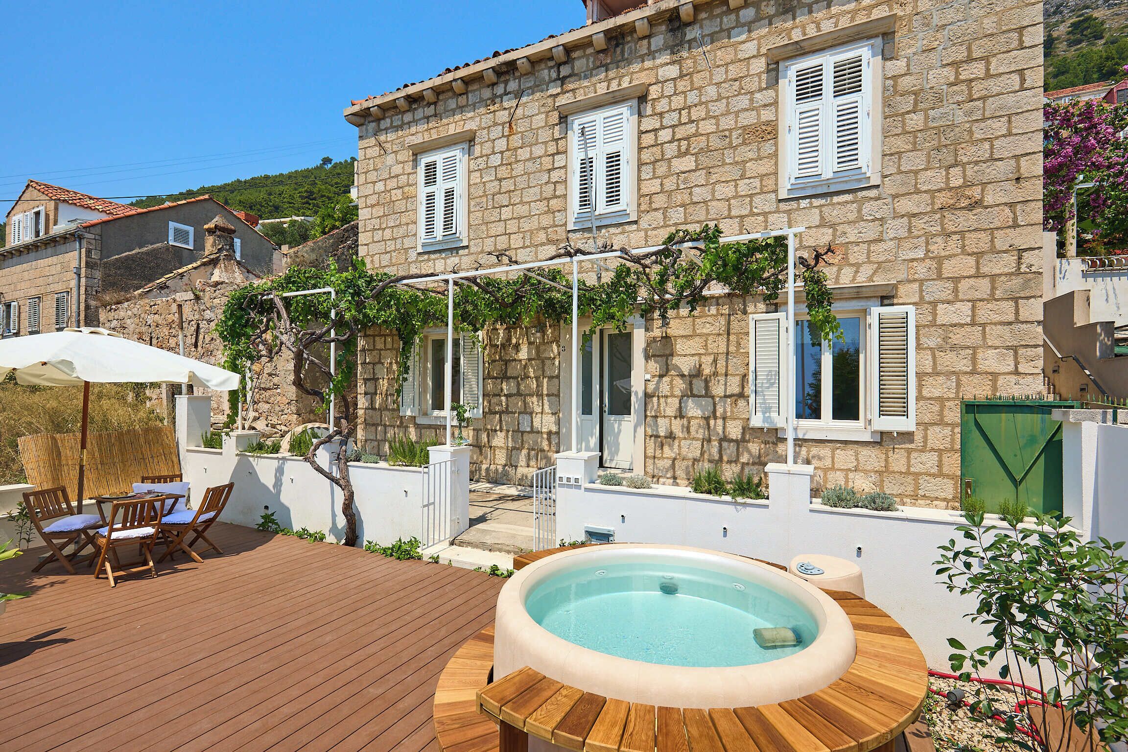 A stone building with a wooden deck, outdoor seating, and a hot tub.