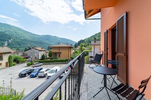 Un balcon avec une table et des chaises, donnant sur une rue bordée de voitures garées et de maisons.