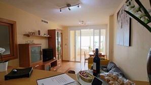 Una sala de estar moderna con televisor, comedor y una mesa de centro de vidrio con pasteles.