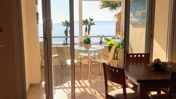Una habitación con puerta de vidrio corrediza que da a un balcón con vista al mar y palmeras.
