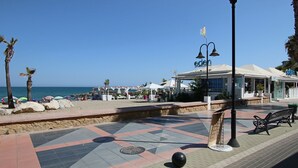 Un paseo marítimo frente a la playa con un café, bancos y una vista despejada del mar.