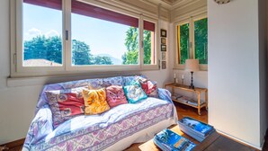 Une pièce chaleureuse avec une grande fenêtre, un canapé agrémenté de coussins colorés, une petite table avec des livres et une lampe.