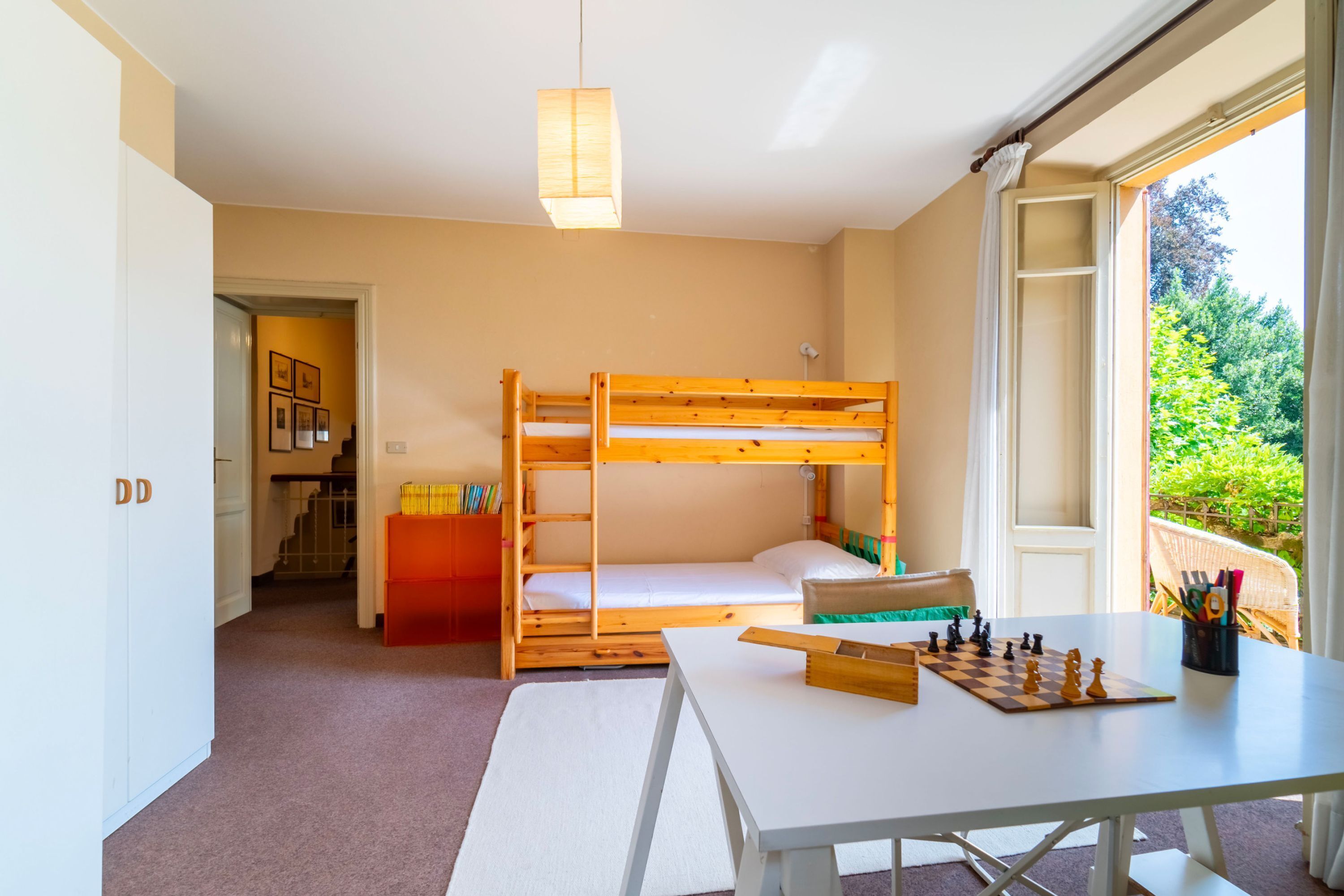 Une chambre avec des lits superposés, une table avec un jeu d’échecs et une fenêtre donnant sur un paysage verdoyant.