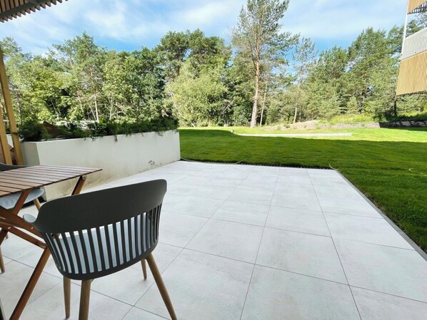An outdoor patio area with a table and chairs, a tiled floor, and a view of a grassy lawn and trees. - Timber Apartments by Baltic Home (Swinoujscie)