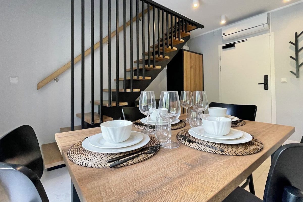 Ein Essbereich mit einem Holztisch, der für eine Mahlzeit gedeckt ist, eine Treppe mit schwarzen Geländern und ein modernes Interieur.