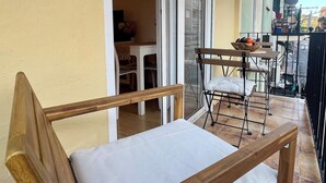 A balcony with a wooden chair, a small table with a bowl of fruit, and a potted plant.