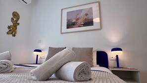Una cama bien hecha con toallas enrolladas, dos lámparas de noche, un cuadro en la pared y un adorno de pared.