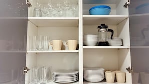 Un armario de cocina con estantes que contienen cristalería, platos y una cafetera.