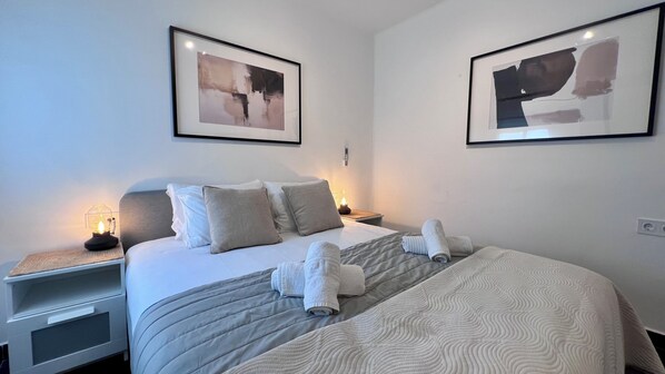 A neatly made bed with pillows and rolled towels, a bedside table with a lamp, and two framed pictures on the wall.