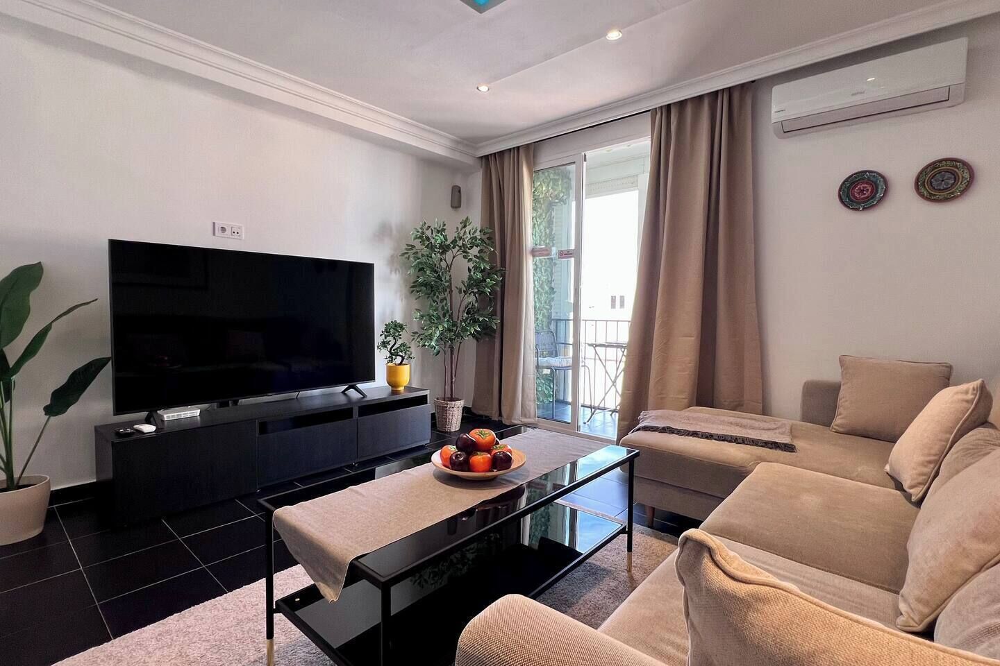 Ein modernes Wohnzimmer mit Flachbildfernseher, Sofa, Couchtisch und einer Zimmerpflanze.