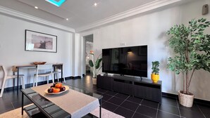 Una sala de estar moderna con un televisor de pantalla plana, un comedor con sillas y una mesa, y una planta en maceta.