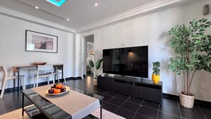 Una sala de estar moderna con un televisor de pantalla plana, un comedor con sillas y una mesa, y una planta en maceta.