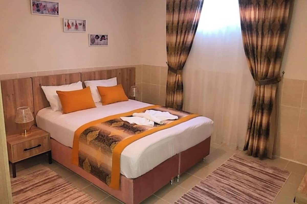 A hotel room with a bed, curtains, a nightstand, and wall art.