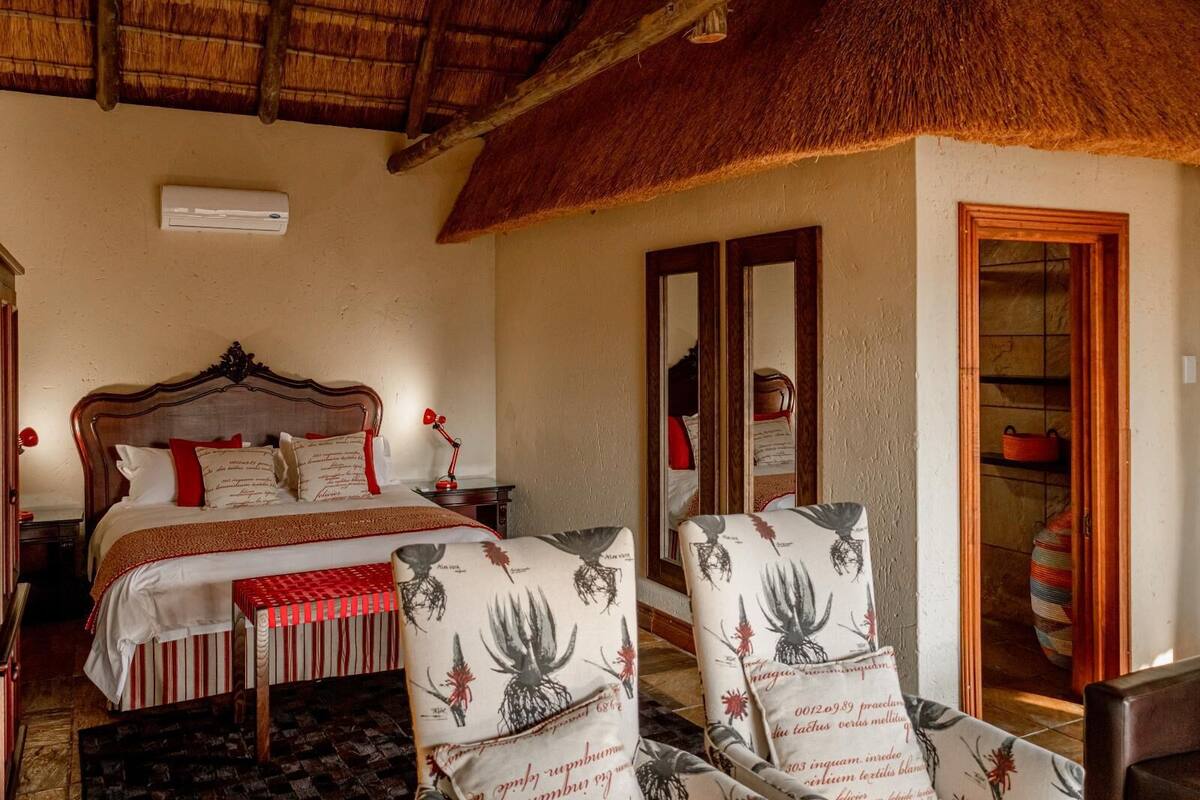 A room with a bed, two armchairs, a mirror, and a door leading to a bathroom.