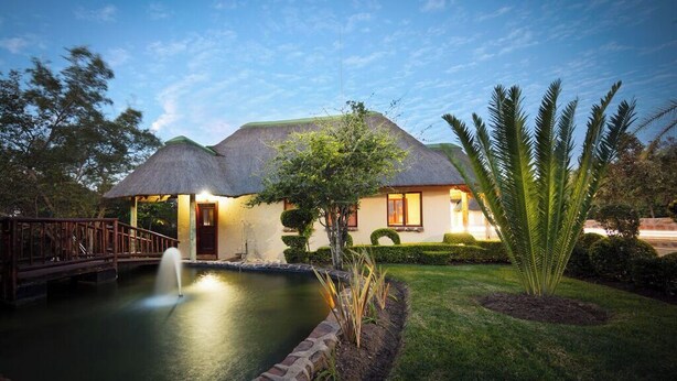 Una casa con techo de paja, piscina y un puente.