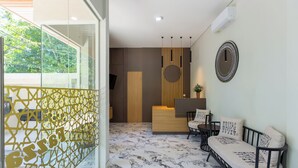 Un área de recepción moderna con un mostrador de madera, un espacio de descanso con sofá y sillones, y un elemento decorativo en la pared.
