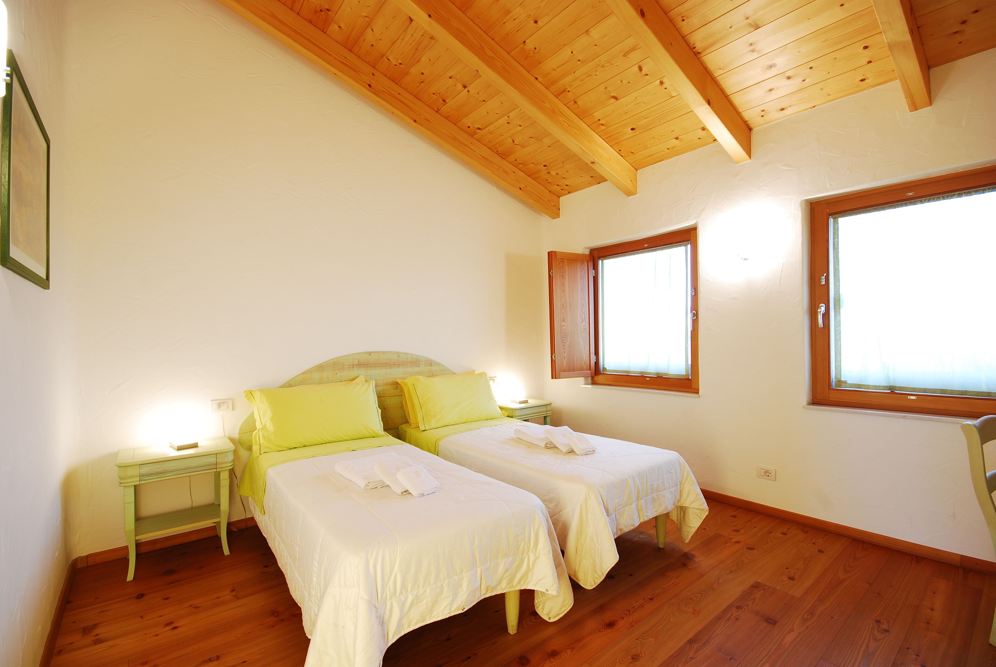 A bedroom with two beds, wooden flooring, a sloped ceiling, and large windows.