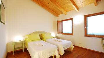 A bedroom with two beds, wooden flooring, a sloped ceiling, and large windows.