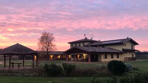 A two-story building with a covered patio area and a gazebo in a grassy field during sunset. - Corte all'Olmo (Verona)