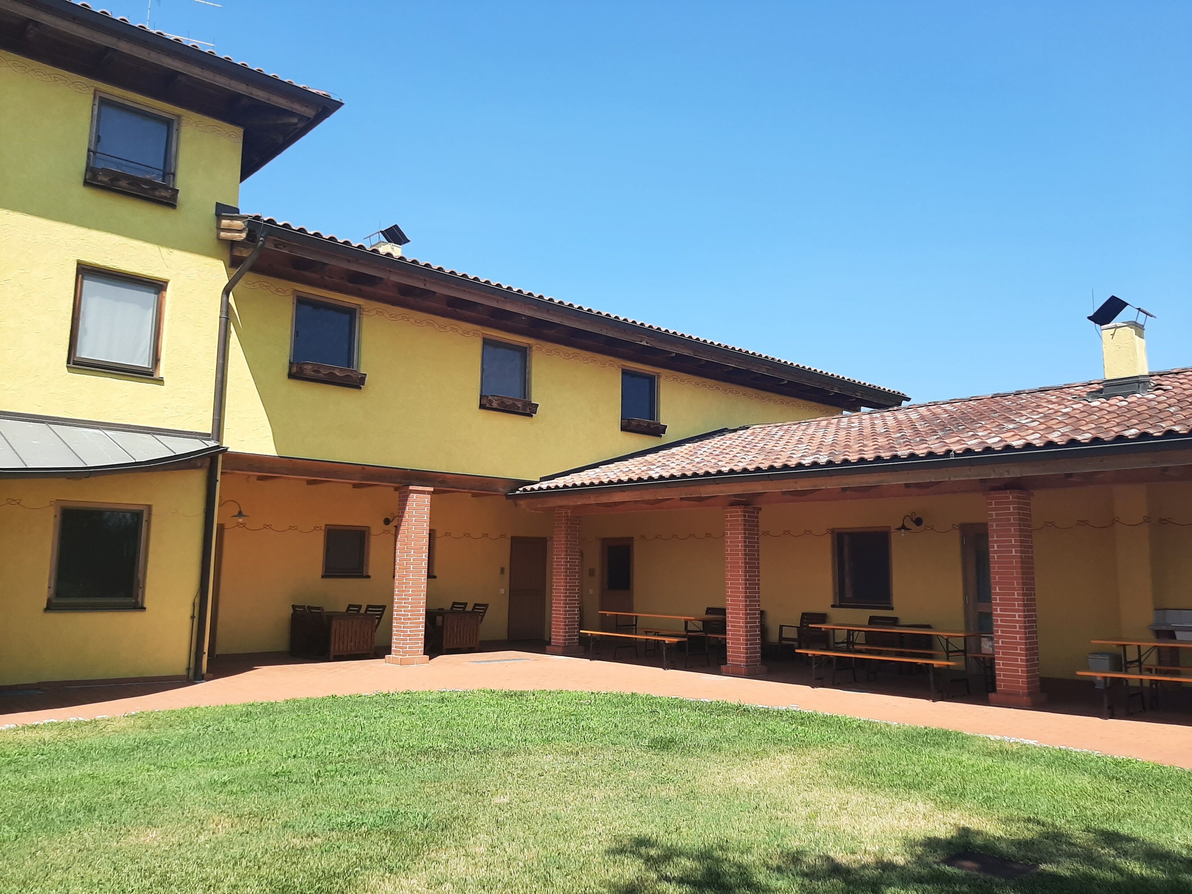 Un patio con un edificio amarillo, pilares de ladrillo y asientos al aire libre.