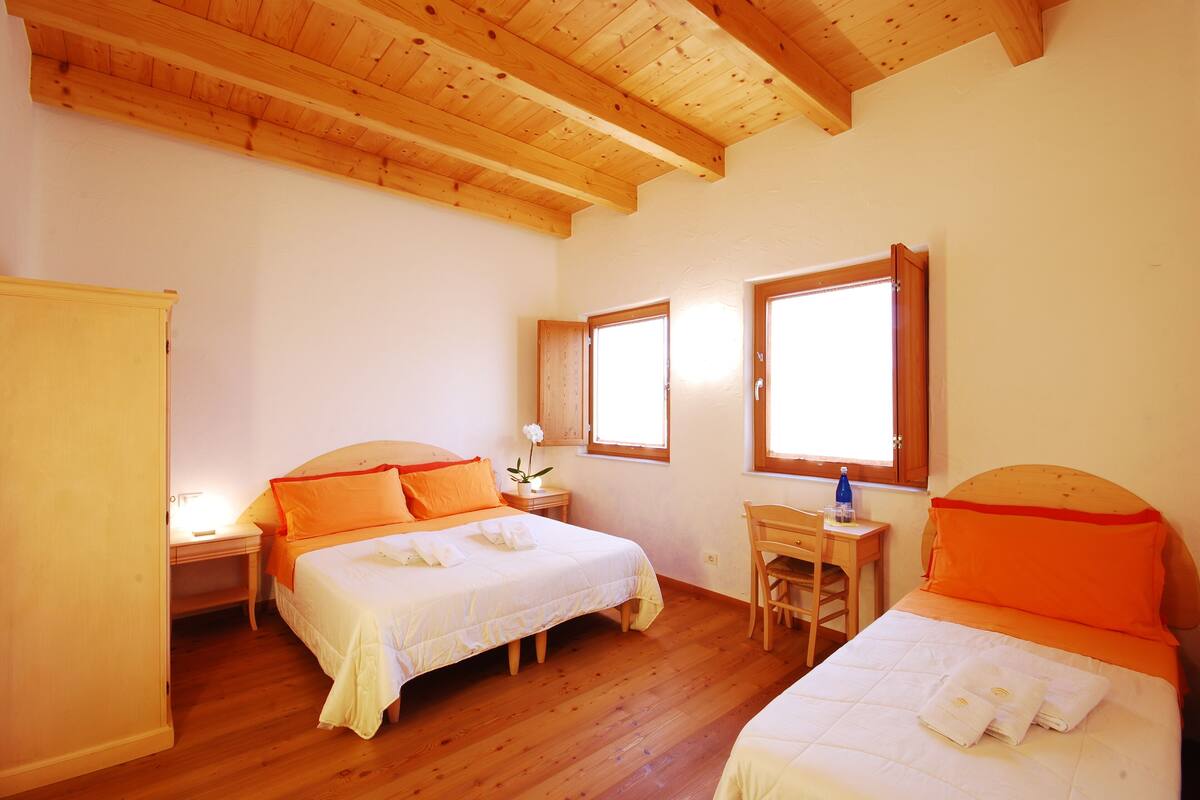 A bedroom with two beds, wooden flooring, and a desk with a chair.