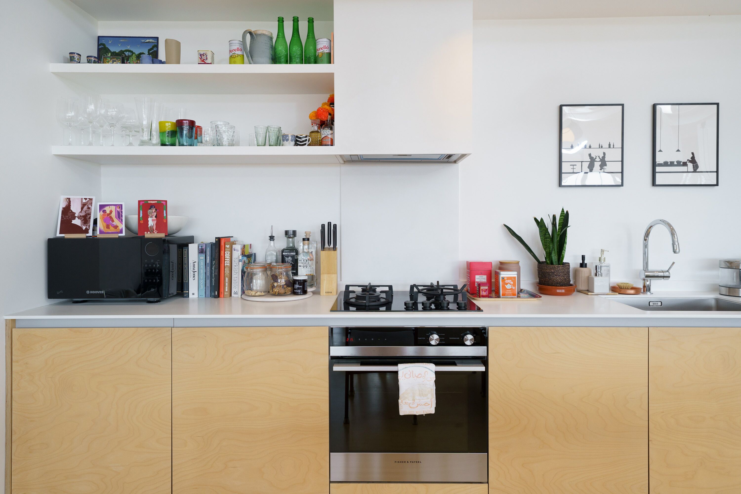 Une cuisine moderne équipée d’un four à micro-ondes, d’une cuisinière, d’un four et d’un évier. On y trouve des étagères où sont rangés de la vaisselle et des objets décoratifs.