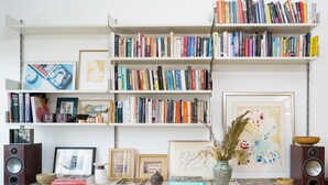 A bookshelf filled with books, a framed picture, and a vase with dried flowers. - Super Spacious Penthouse in Art Deco Warehouse Conversion (London)