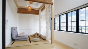 A minimalist room with tatami mats, a low wooden platform, a grey sofa, and a large window offering a city view. - Super Spacious Penthouse in Art Deco Warehouse Conversion (London)